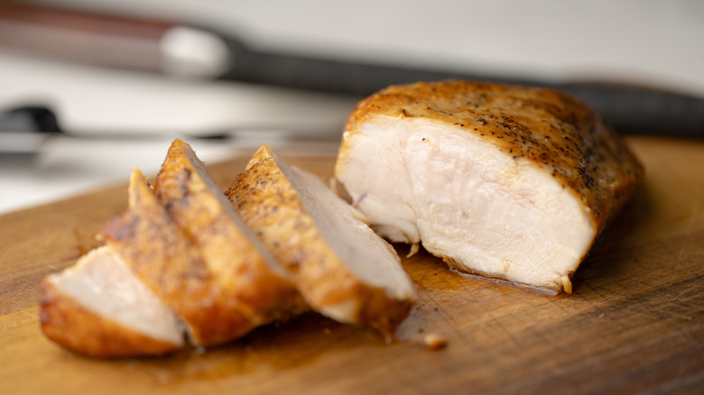 Close up of sliced seared chicken breast on wooden cutting board