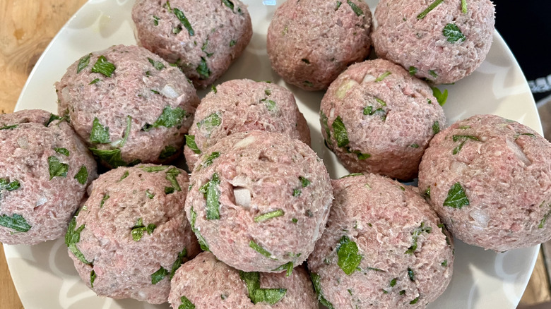 uncooked meatballs with herbs and onion on a white plate