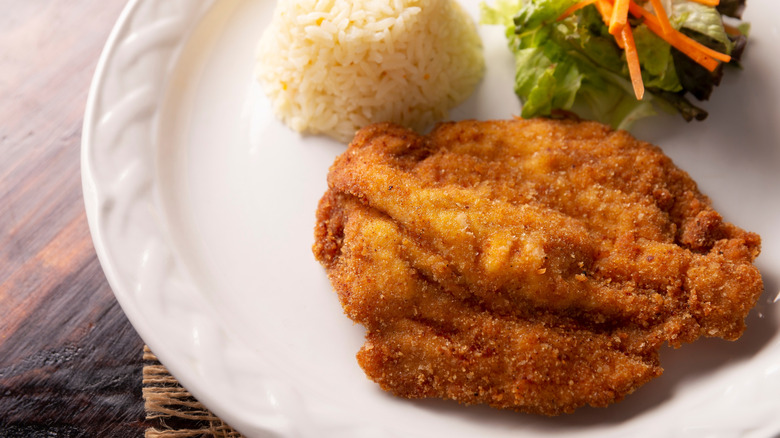 butterflied chicken breast Milanese, served on a white plate with a molded scoop of rice and small green salad