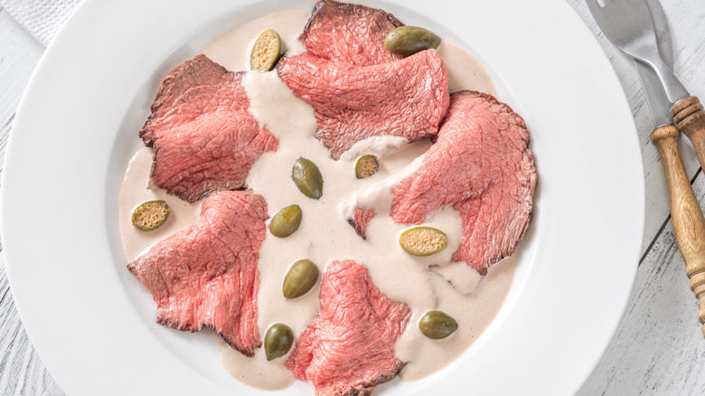 Italian appetizer, vitello tonnato, of thin-sliced veal with tuna-based sauce, shown on a white plate with a garnish of capers