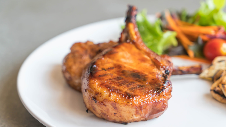 pork rib chops on a white plate, with a salad visible in soft focus to the rear