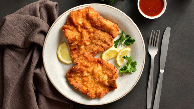 pork schnitzel on a white plate, with lemon and parsley garnishes