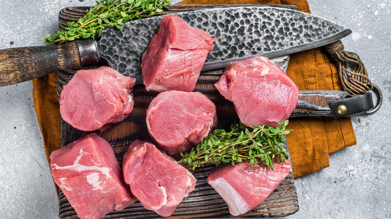 fresh pork tenderloin medallions, shown on a cutting board with bundles of thyme and an exotic-looking knife with a dimpled blade
