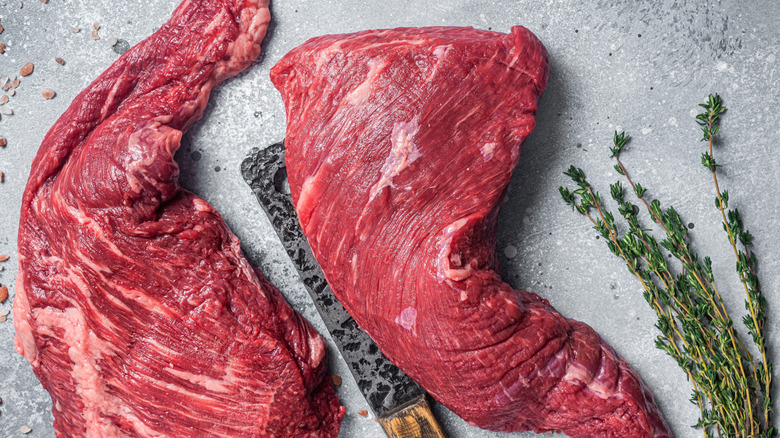 raw sirloin tip shown on a grey stone countertop with coarse pink salt, thyme sprigs and a knife