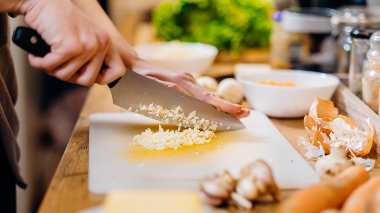 Knife mincing garlic on board