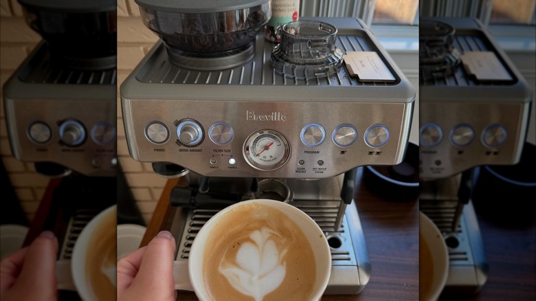 Person holding a cup of coffee with latte art in front of a Breville Barista Express