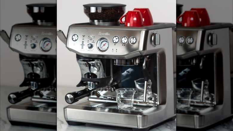 Silver Breville Barista Express Impress with full coffee grinder and two upside down red coffee mugs sitting on top of machine