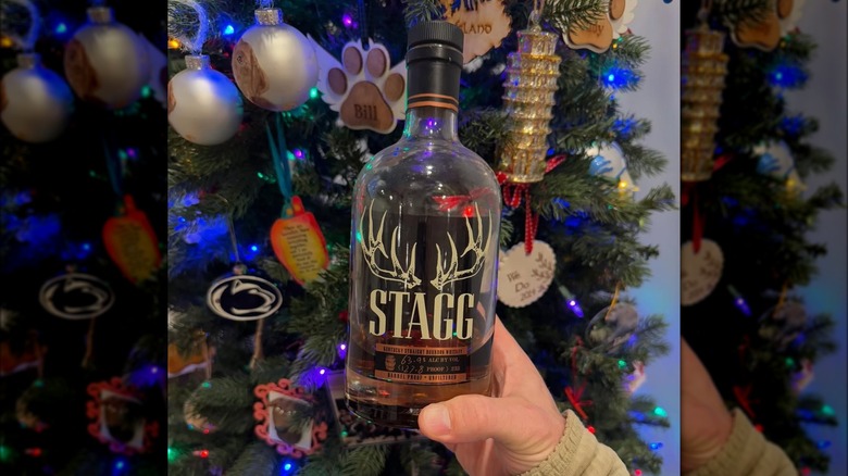 Hand holding a bottle of Stagg Bourbon by a Christmas tree