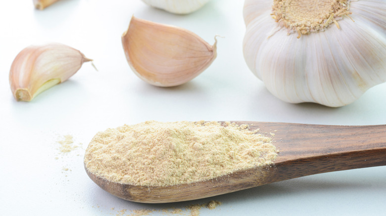 Garlic powder in a wooden spoon surrounded by fresh, whole garlic