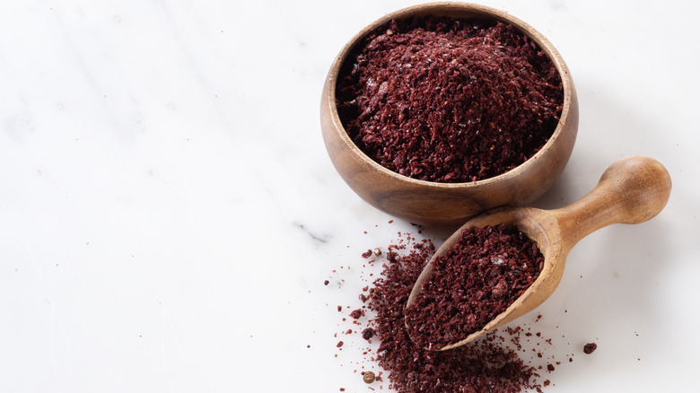 Sumac spice in a wooden bowl and spoon with white background