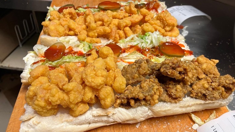 Open-faced po'boys with fried seafood on cutting board in kitchen