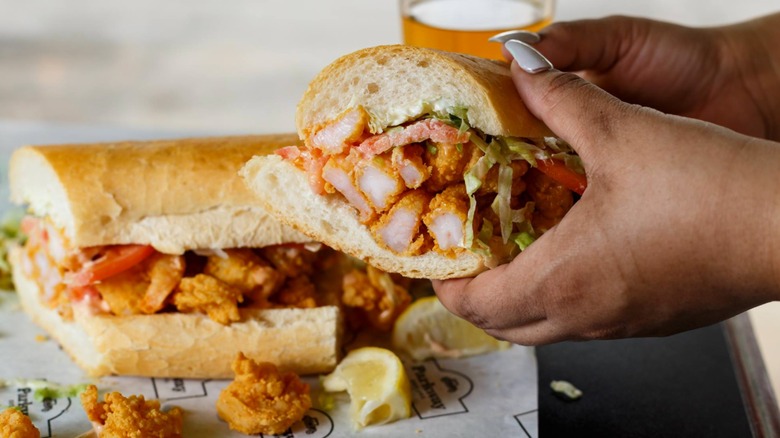 Woman's hands hold fried shrimp sandwhich on Parkway Bakery paper with beer in background