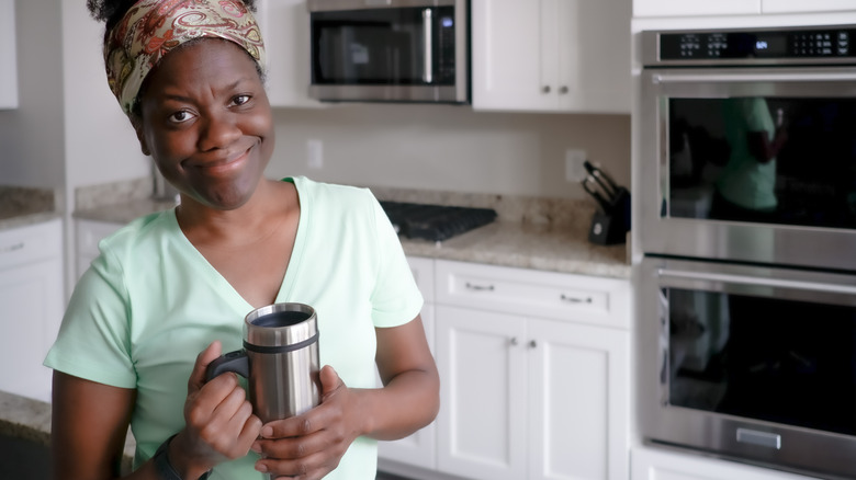 Woman smiling and holding a travel mug in a kitchen