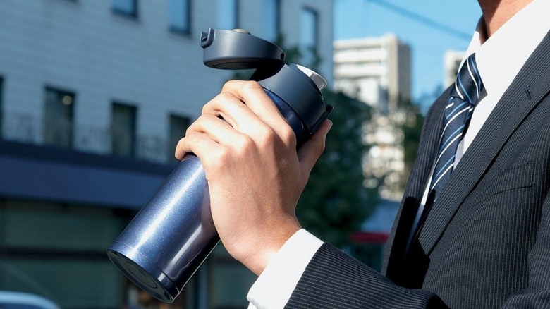Man in a suit and tie holding a Zojirushi travel mug outside