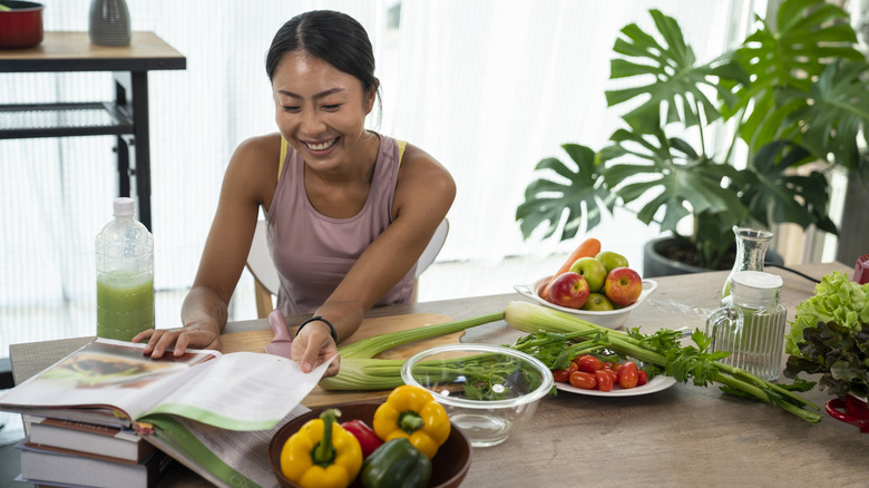 woman looking through cookbooks at a table covered in vegetables