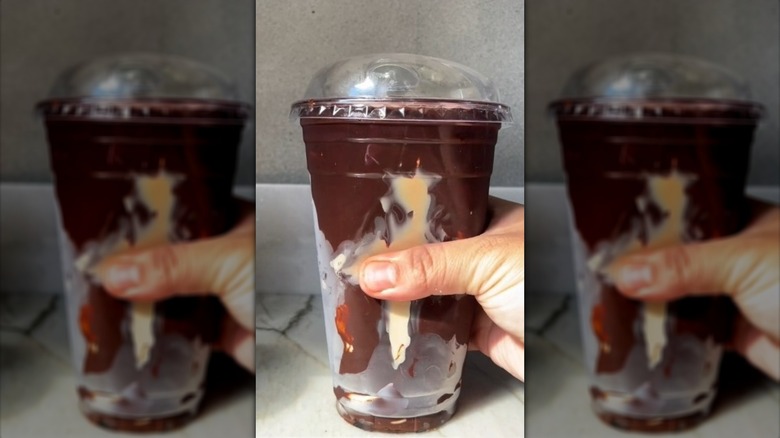 Hand holding cracking chocolate latte in a plastic cup