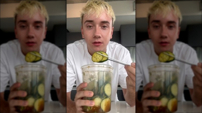 Man eating cucumber salad from a plastic tub with chopsticks