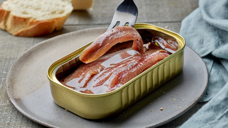 Canned anchovies being removed with a fork on a plate