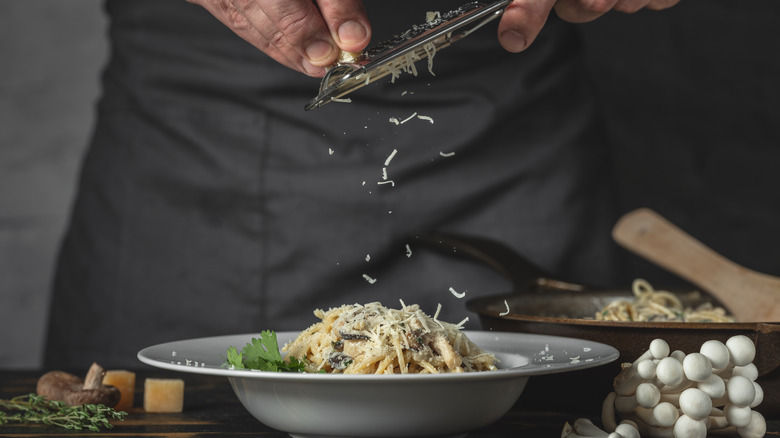 Person grating Parmesan cheese over bowl of pasta