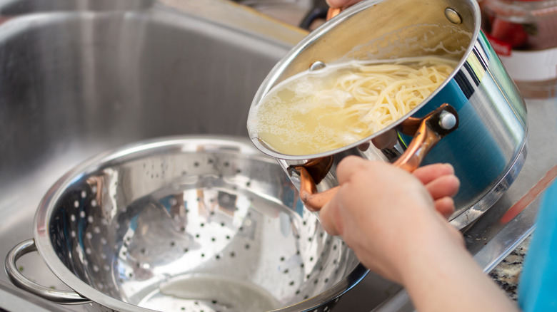 Person draining cooked pasta in a colander at the sink