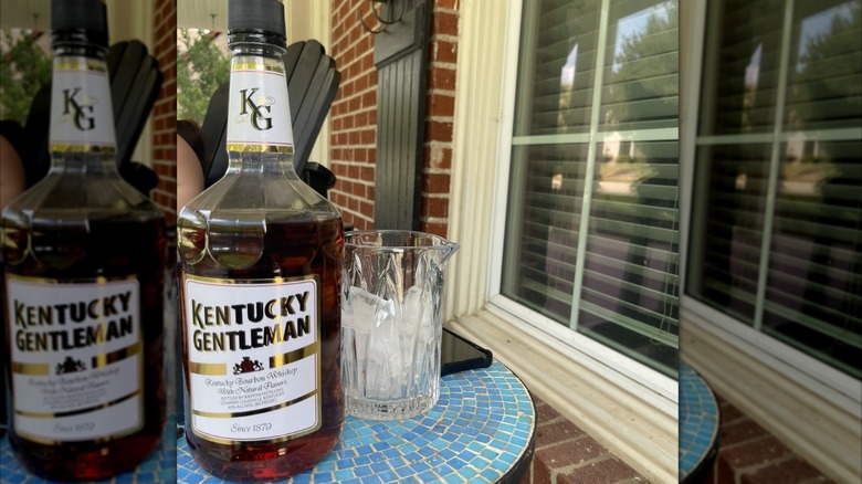 Bottle of Kentucky Gentleman on a blue mosaic table with a glass on the side and a porch in the back