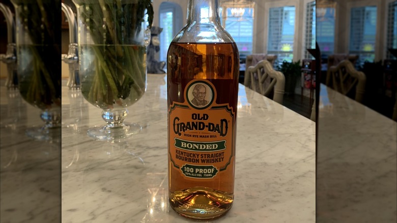 Bottle of Old Grand-Dad bourbon on a marble counter with a vase in the back