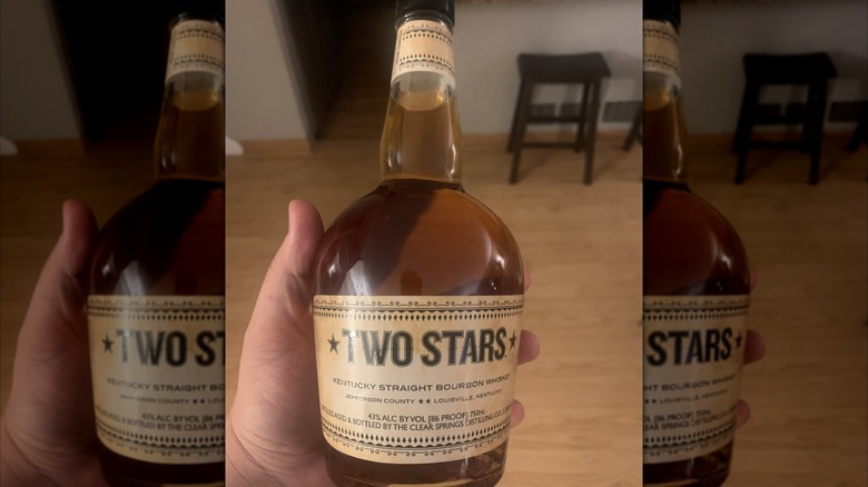 A person holding a bottle of Two Stars bourbon