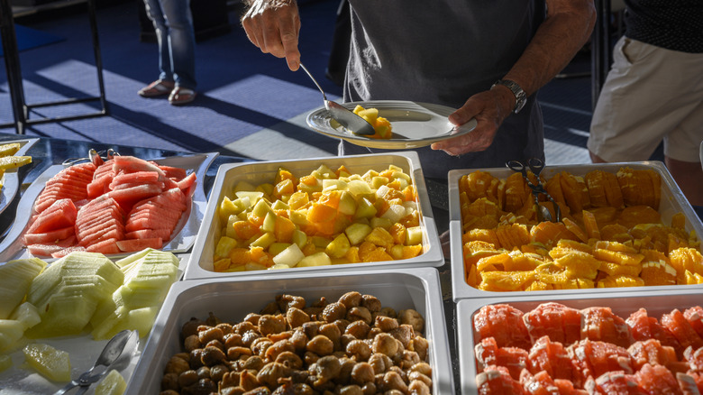 Person plating fresh fruit offerings at a buffet