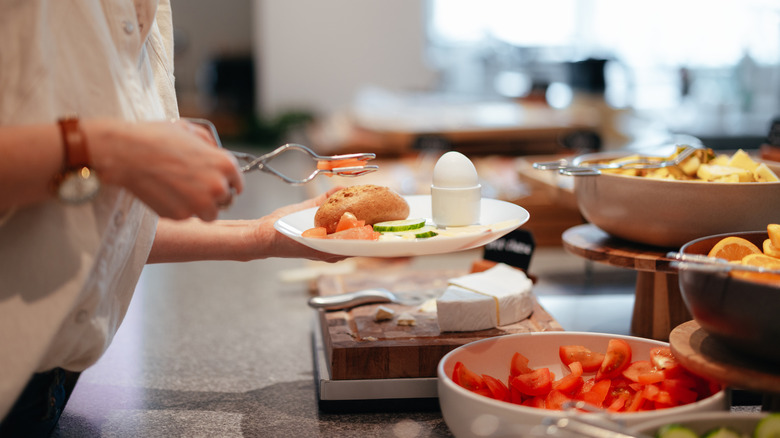 Person stacking food on a plate at a breakfast buffet