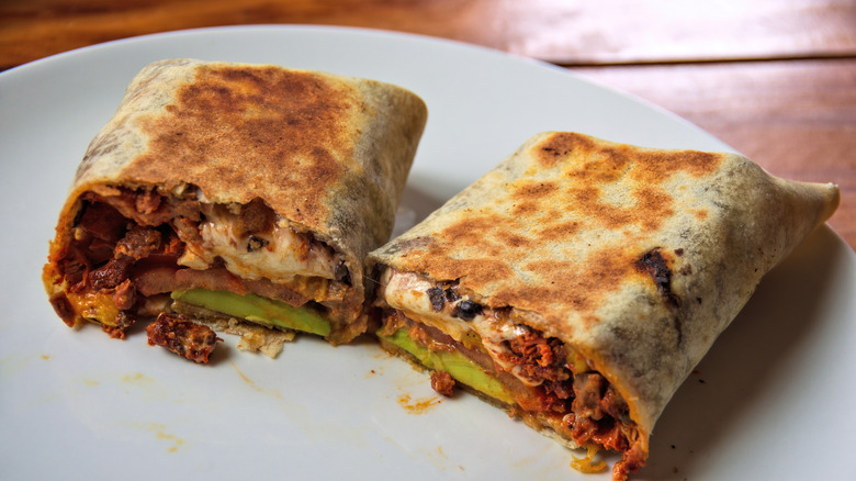 A breakfast burrito cut in two on a white plate to showcase the filling