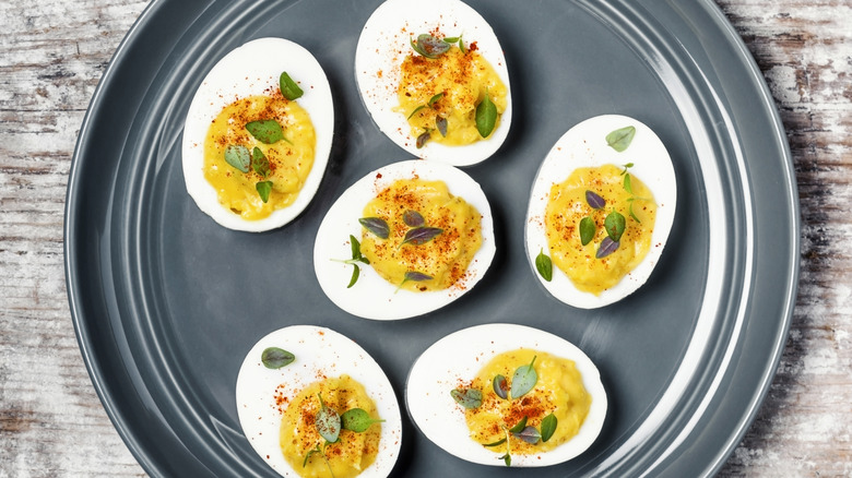 Top view of six deviled eggs sitting on a dark plate sprinkled with leafy greens and paprika