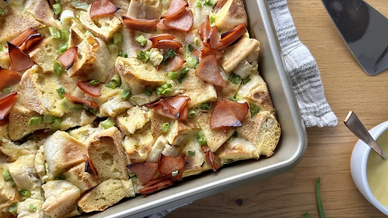 A tray of baked eggs benedict casserole with hollandaise on the side