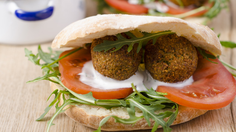 Open pita bread pocket filled with falafel, arugula, tomatoes, and a white sauce sitting on a wooden counter