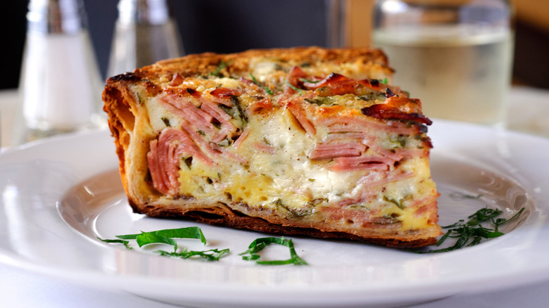 Slice of ham and cheese quiche on a white plate