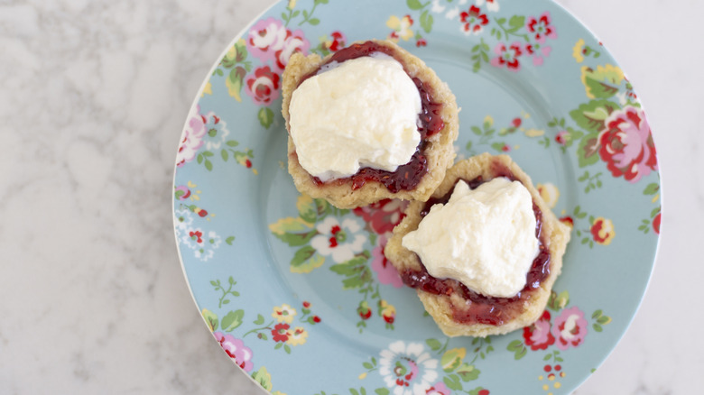 Top view of open scone with jam and cream on a flowery plate with a white marble counter in the back