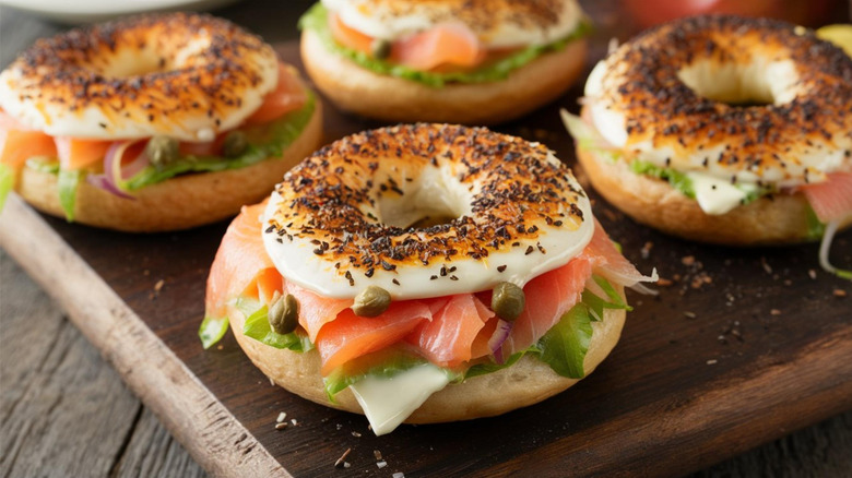 Four smoked salmon bagels with cheese, capers, onions, and salad on wooden board