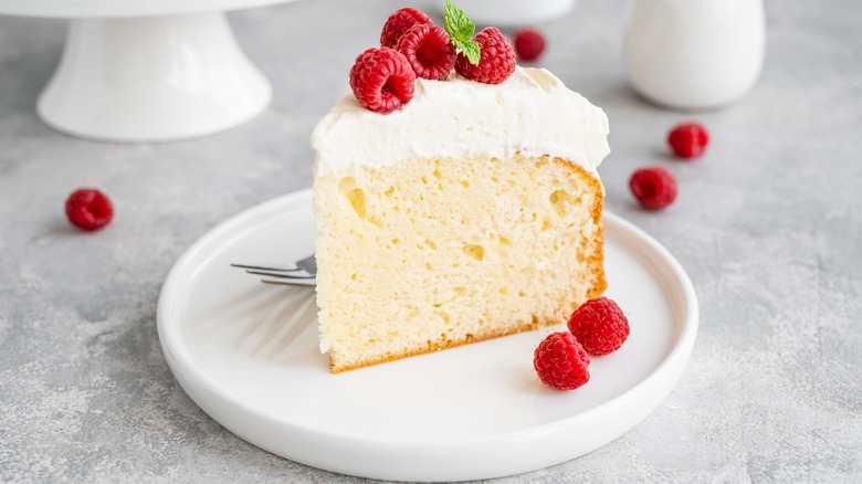 Slice of tres leches on a white plate with raspberries