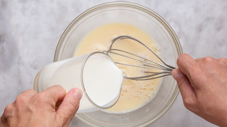 person pouring milk into bowl of batter and whisk