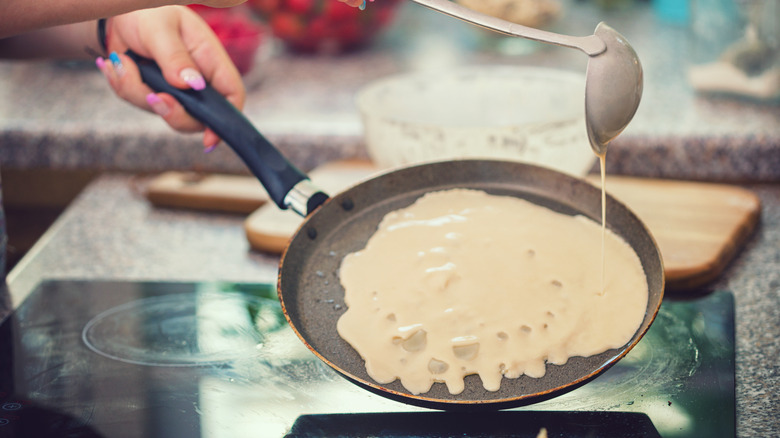 person drizzling crepe batter while holding pan handle