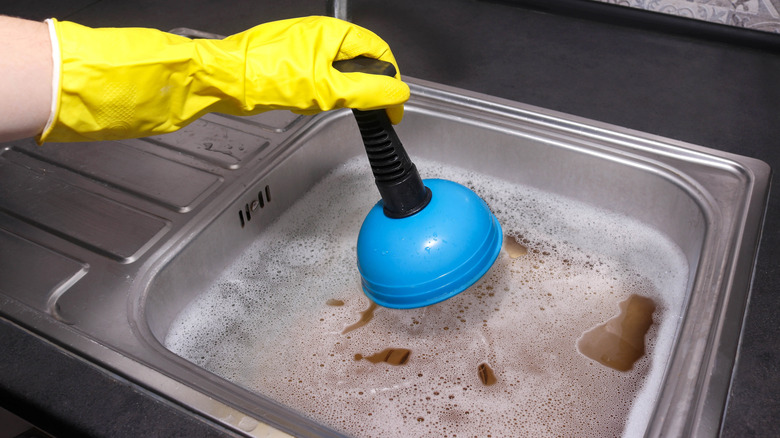 A person using a plunger to unclog a kitchen sink