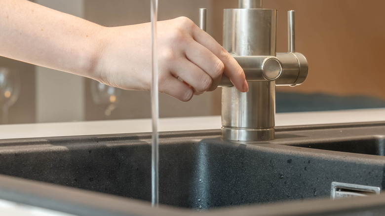 A person turning on the kitchen sink
