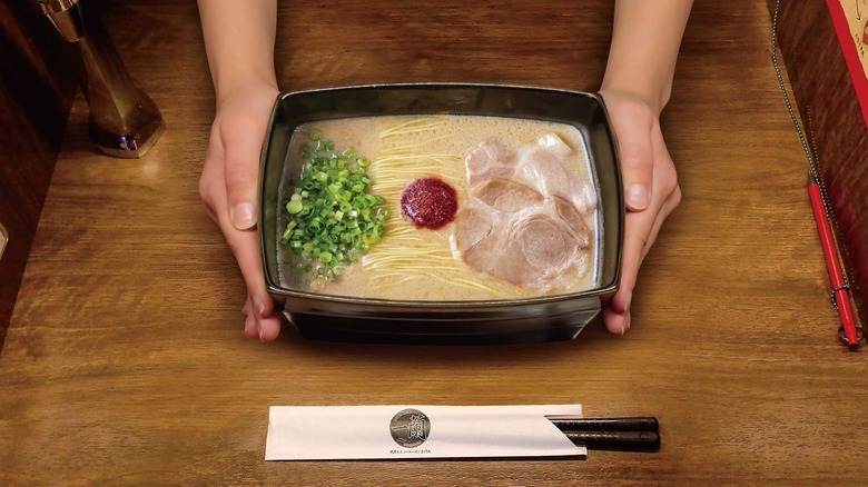 Two hands holding ramen dish