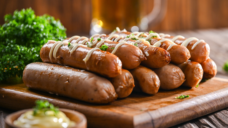 Chopping board stacked with sausages drizzled with mayonnaise