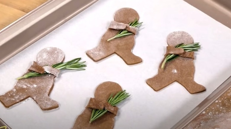 Unbaked gingerbread men with folded arms holding rosemary sprigs