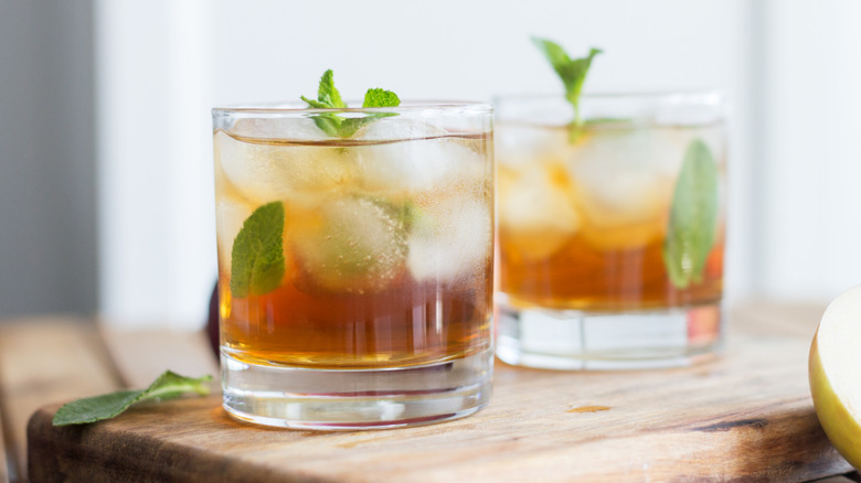 Two cocktails with mint and ice on wooden cutting board