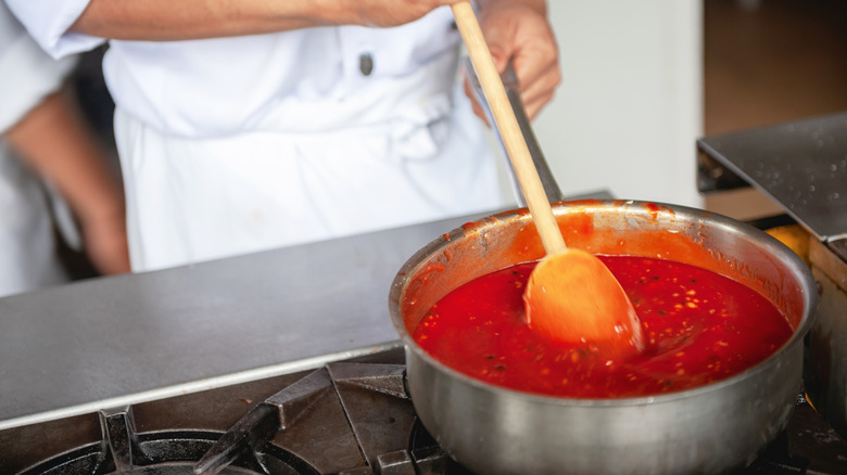 Chef stirring pasta sauce in metal pot