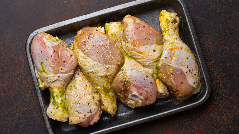 Raw chicken drumsticks in marinade in black pan
