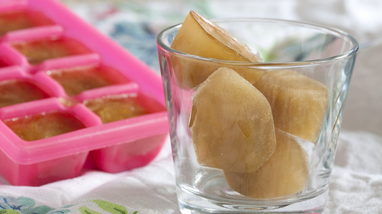 Broth frozen into ice cubes packed in a glass with a pink ice tray in the back