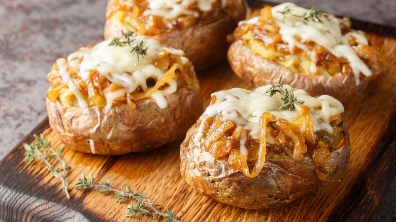 Baked potatoes on a wooden board filled with french onion soup, topped with cheese, and garnished with a thyme