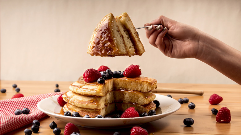 fork holding piece over plate of fluffy pancakes